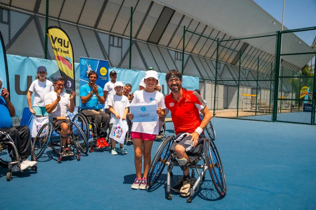 Momento del torneo en pista: participantes, niña con diploma y jugador en silla, UPV al fondo
